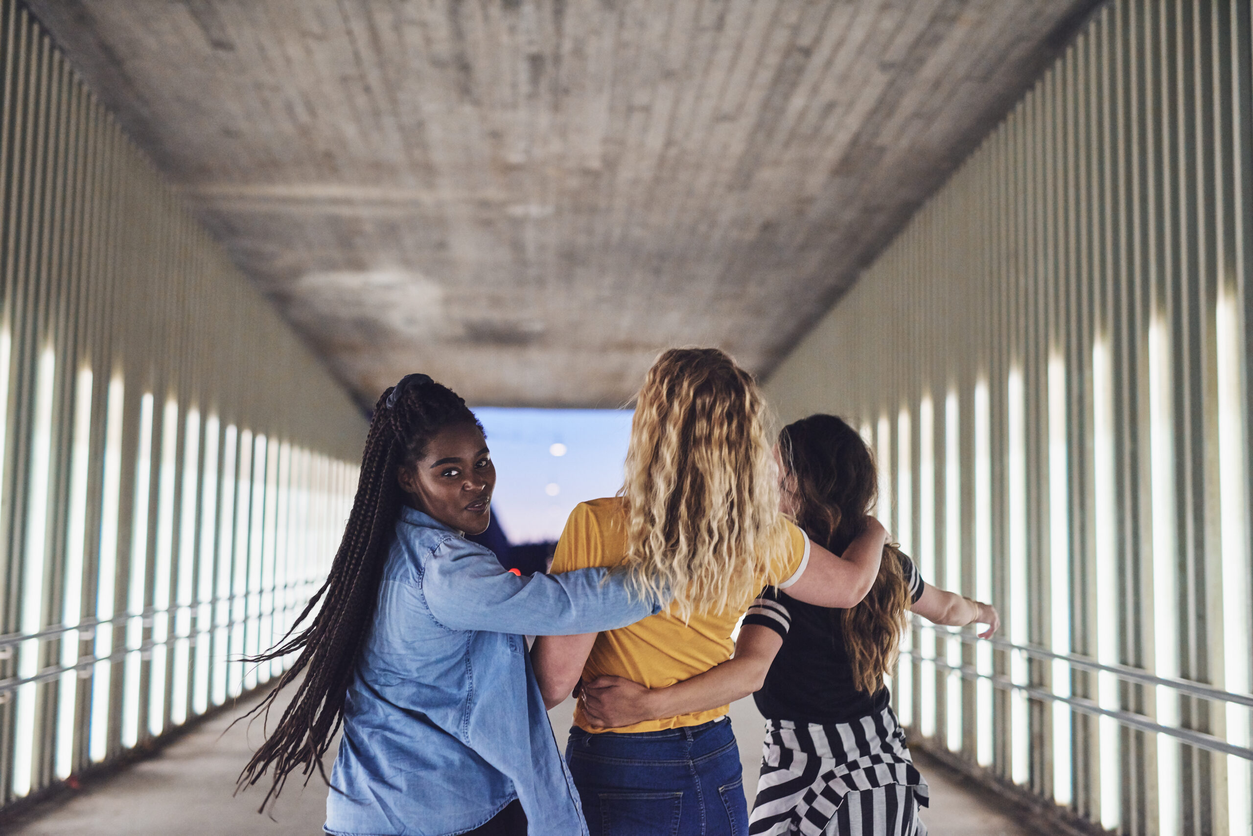 Carefree group of diverse young girlfriends having fun while walking arm in arm together down a walkway in the city at night