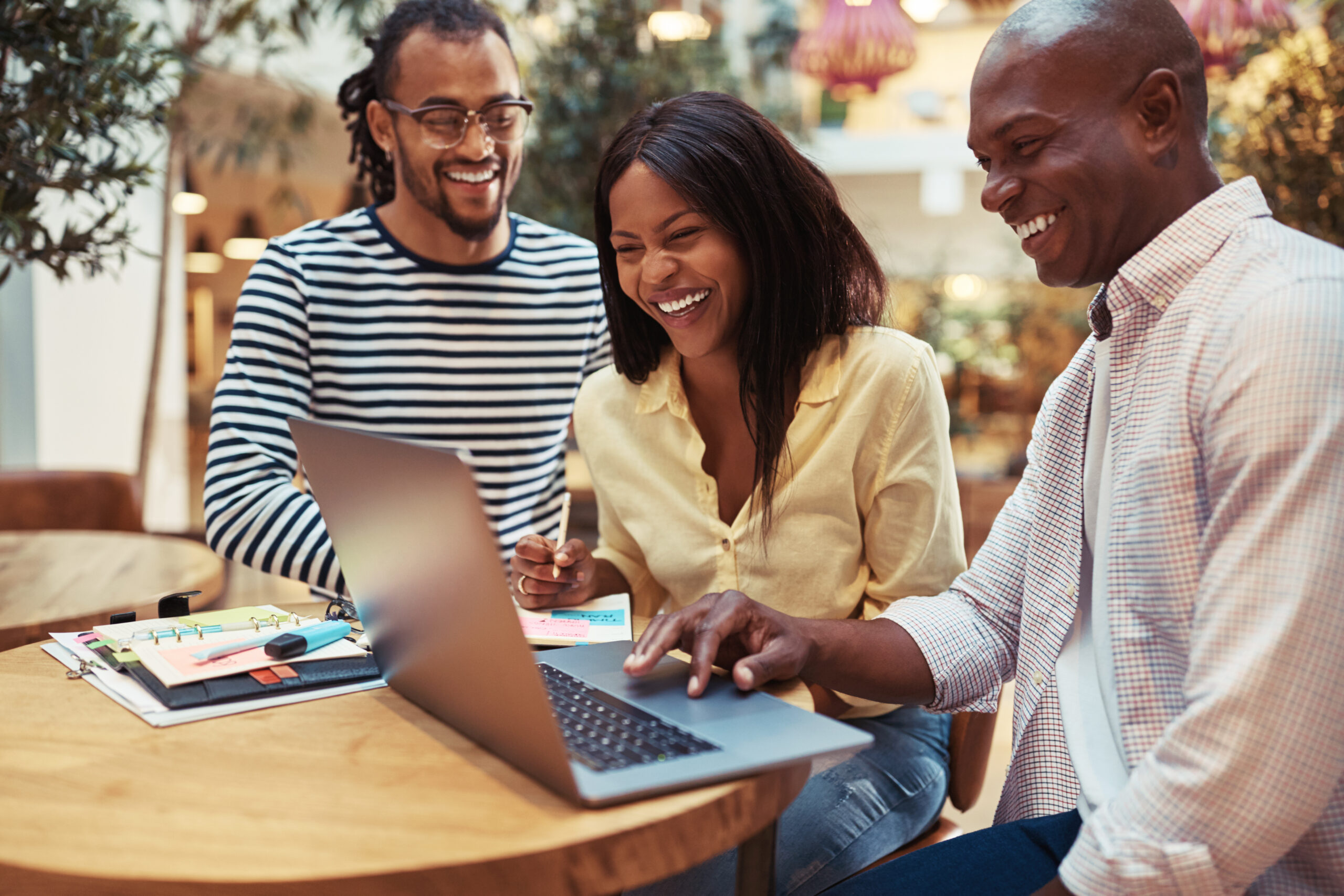 Group of laughing young businesspeople working on a laptop while sitting together at a table in an office lounge