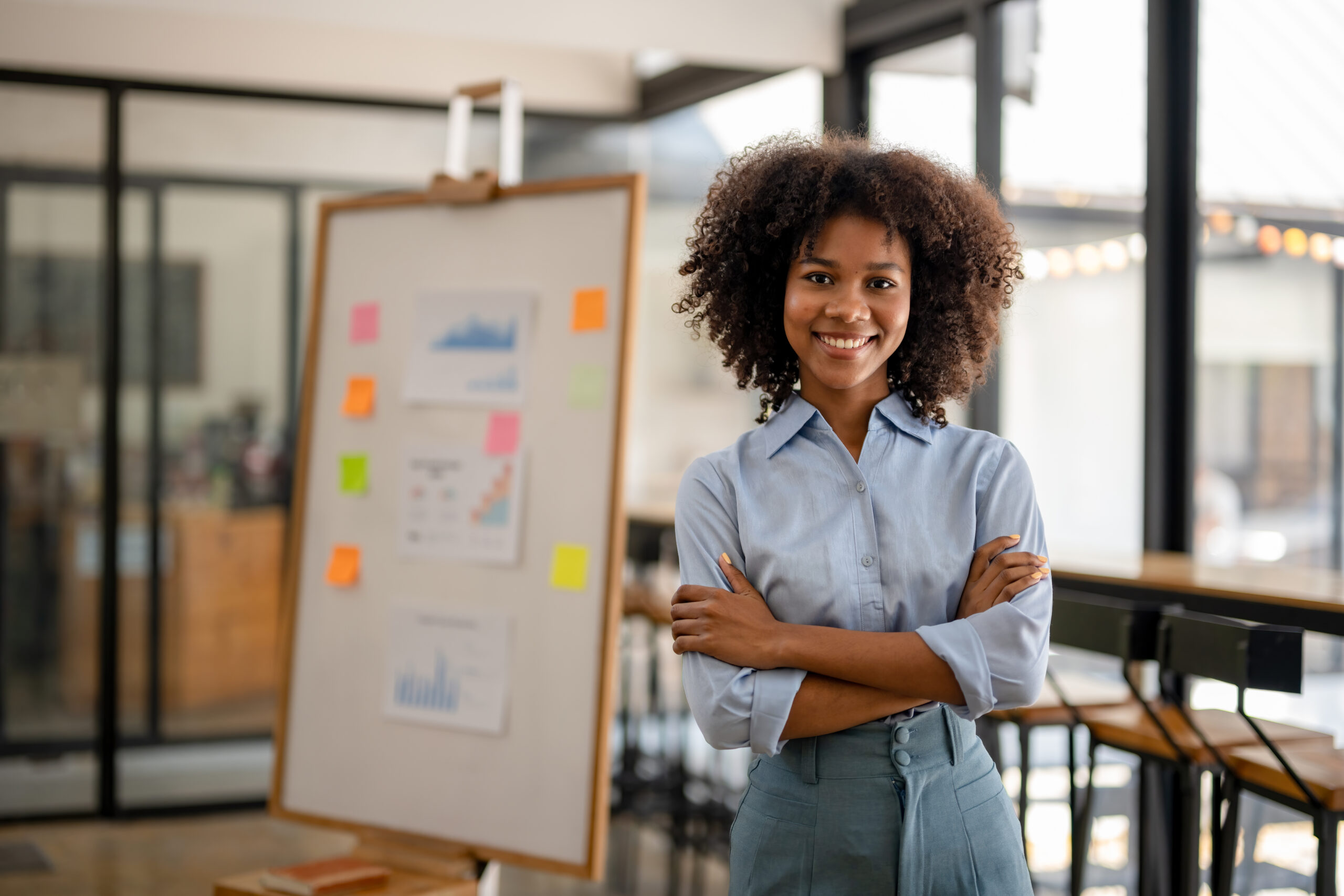 Portrait of beautiful happy black woman standing with arms crossed, business woman standing confidently with arms folded at the workplace